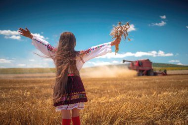 Hasat zamanı tarım buğday tarlasında geleneksel Bulgar folklor kostümlü genç kız sanayi makinesiyle birleştirildi