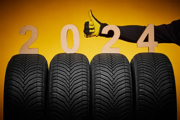 Winter car tires service and thumb up hand of mechanic and text 2024 happy new year on yellow background.