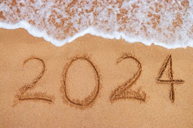 Mutlu yıllar 2024 konsepti, plajda yazı yazmak. Gün doğumunda sahilde yazılmış bir metin..