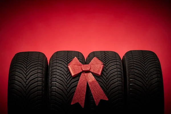 車のタイヤ 新しいタイヤ 弓のリボンが付いている赤いクリスマスの背景で隔離される冬の車輪 — ストック写真
