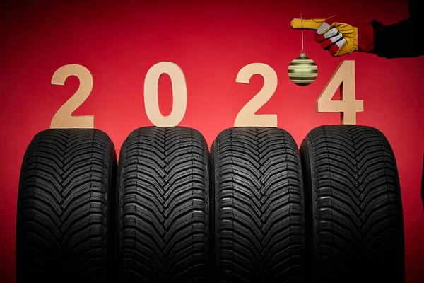 Winter car tires, big wheels service and hand of mechanic man with wrench and christmas tree ball on red new year 2024 background