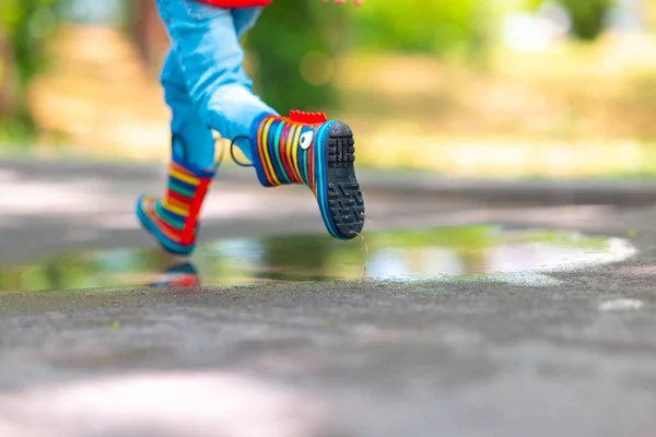 穿着彩色橡胶雨靴的孩子的脚跳过公园里的水坑 — 图库照片