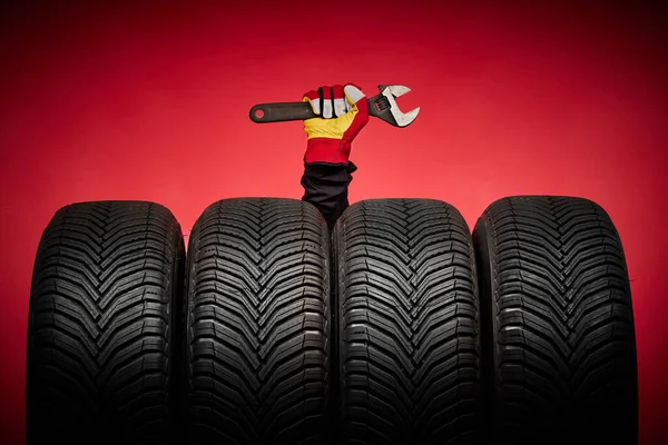 Car tires service and hand with wrench of mechanic man on red background, safety racing and good wheels concept.