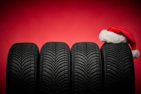 Winter car tires, big wheels and Santa Claus hat christmas red background