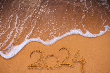 Mutlu yıllar 2024 konsepti, plajda yazı yazmak. Gün doğumunda sahilde yazılmış bir metin..