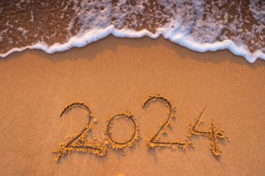 Mutlu yıllar 2024 konsepti, plajda yazı yazmak. Gün doğumunda sahilde yazılmış bir metin..