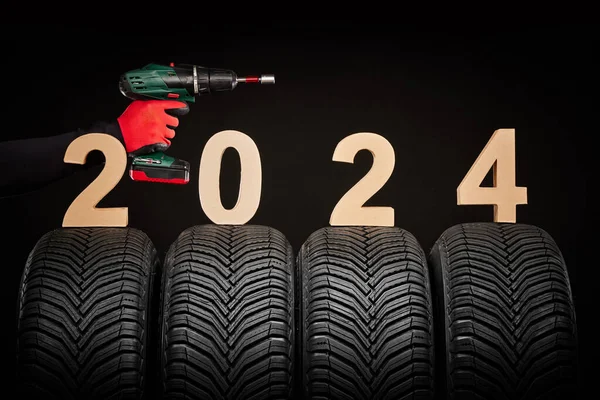 冬の車のタイヤ タイヤ サービス 車輪のためのドライバーが付いている修理人手 2024幸せな新年の黒い背景 ロイヤリティフリーのストック画像
