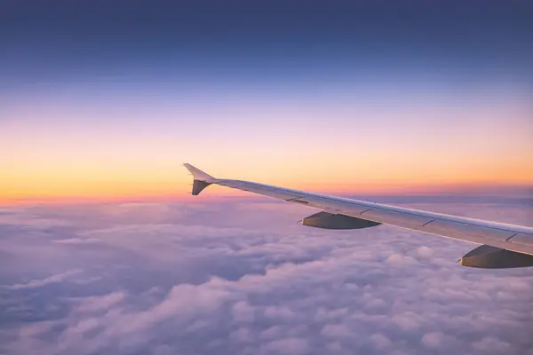 飞机在日落或日出时飞越彩云 从机翼涡轮机和地平线的平面窗口看风景 图库图片