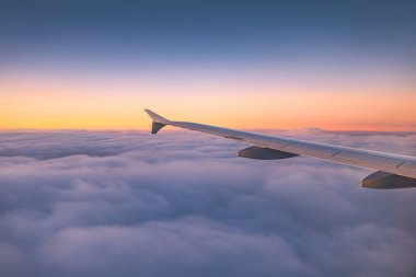 Renkli gökyüzü bulutları üzerinde uçan uçak manzaralı günbatımı veya gündoğumu bulutları, kanat türbinlerinin uçak penceresinden ve ufuk çizgisinden manzara