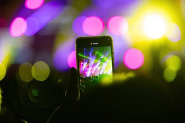 Sahne ışıkları, canlı yayını kaydeden akıllı telefon videosuyla birlikte bir müzik konserinde arka planlarını bozar.
