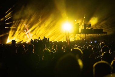 Sahne ışıkları, bir müzik konserinde arka plandaki bokeh örtüsünü ve kalabalığın içindeki insanları kutlayan siluetleri çözer.