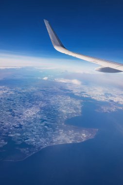 Güneşli bir günde karlı dağların üzerinde uçan uçaklar, bulutların ve kanat türbinlerinin uçak penceresinden manzara