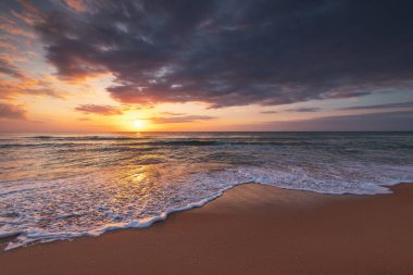 Deniz ufkunda dramatik bulutlar ve gün doğumunda egzotik plajlar.