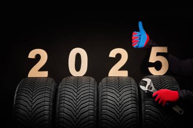 Kışlık araba lastiği servisi ve tamircinin elleri ve 2025 sayılı mutlu yıllar siyah arka planda.