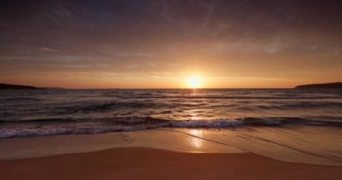 Okyanus kıyısında gün batımı ve kumlara vuran dalgalar. Deniz doğumu videosu