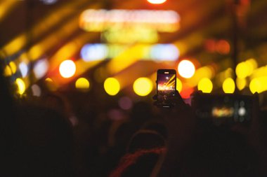 Sahne ışıkları, canlı yayını kaydeden akıllı telefon videosuyla birlikte bir müzik konserinde arka planlarını bozar.