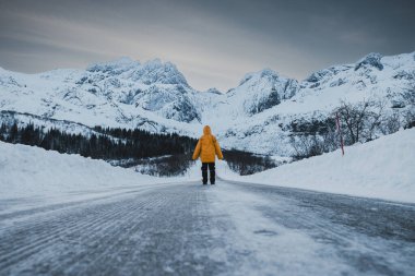 Arktik Kış Manzarası 'nda Karlı Dağ Tepeleri' ne giden donmuş yolda araba izleri ve tırmanışa giden kişi. Lofoten, Norveç