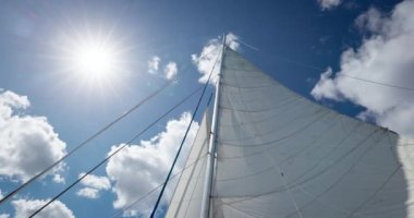  Güneş mavi gökyüzü ve beyaz bulutlarla yelkenli direğinde parlıyor.