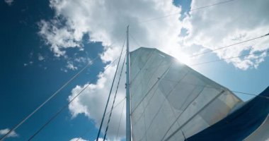  Güneş mavi gökyüzü ve beyaz bulutlarla yelkenli direğinde parlıyor.