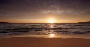 Güzel sahil üzerinde altın gün doğumu ve deniz kumlarını yıkayan sakin su dalgaları.