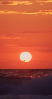 Portakal rengi güneş doğuyor, sabah deniz manzarası boyunca okyanus dalgaları üzerinde bulutlar var.