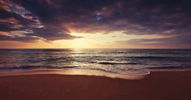 Okyanus dalgaları ve kumlu sahillerde dramatik gökyüzü bulutları altında tropik manzaralı günbatımı