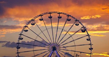 Lunaparkta karnaval dönme dolap ve gökyüzünde gün batımı bulutları