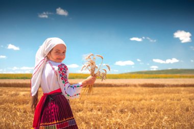 Geleneksel etnik folklor kostümü giymiş Bulgar nakışlı kız altın buğday tarlasında duruyor