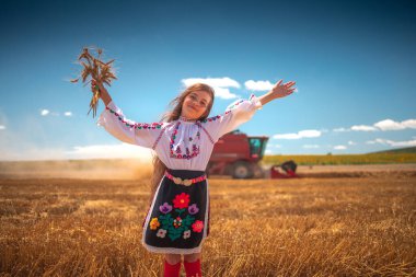 Hasat zamanı tarım buğday tarlasında geleneksel Bulgar folklor kostümlü genç kız sanayi makinesiyle birleştirildi