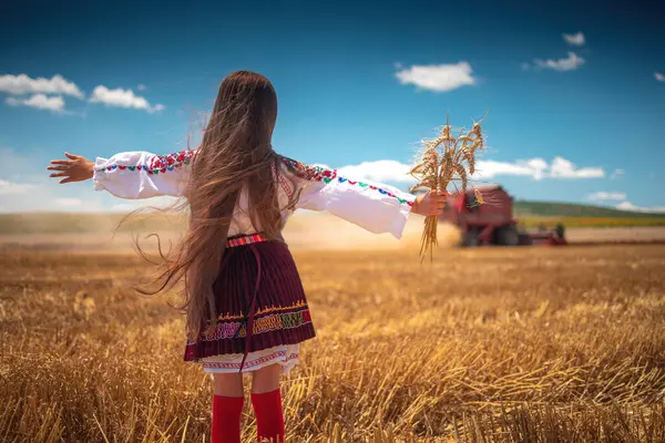 Hasat zamanı tarım buğday tarlasında geleneksel Bulgar folklor kostümlü genç kız sanayi makinesiyle birleştirildi