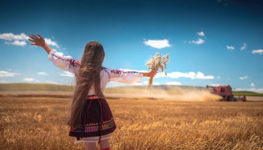 Hasat zamanı tarım buğday tarlasında geleneksel Bulgar folklor kostümlü genç kız sanayi makinesiyle birleştirildi