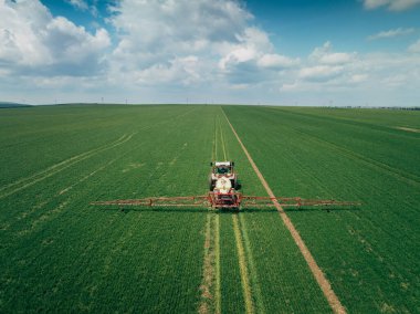 Taze yeşil alanda tarla süren ve püskürten tarım traktörünün hava görüntüsü.