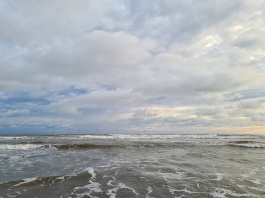 Bulutlu gökyüzü arka planına sahip kahverengi fırtınalı okyanus suyu