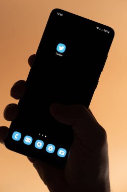 New York, ABD - 4 Kasım 2022: Kahverengi arka planda izole edilmiş akıllı telefon tutarak twitter uygulaması