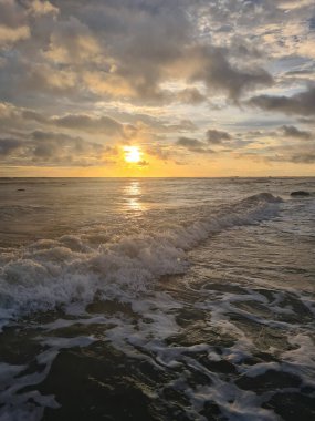 Okyanus dalgası üzerinde yansıması olan turuncu renkli günbatımı
