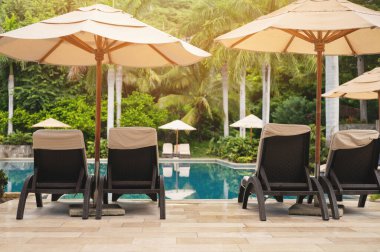 Güneşli bir günde otel havuzunun yanındaki sandalye ve şemsiye.