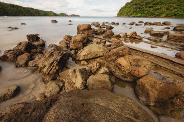 Gün batımında okyanus sahillerinde kayalar yumuşak deniz dalgalarıyla