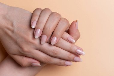 Kadının elindeki güzel tırnaklar bej renkli arka planda görüntüyü kapatır