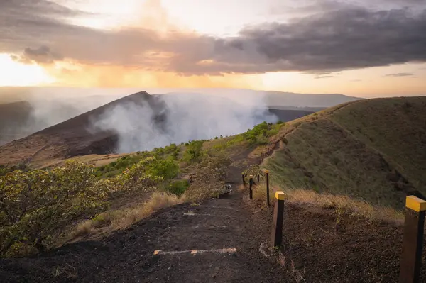 stock image Hiking path in volcano crater with smoke going up on sunset light time