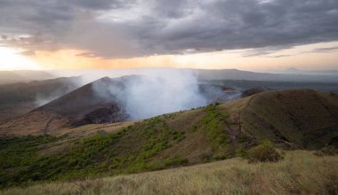 Günbatımı arka planında aktif volkan ve dumanlı manzara 