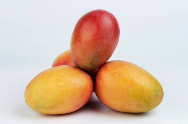 Beyaz stüdyo arka planında tropik turuncu mango meyveleri üst üste yığılıyor.