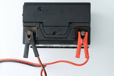 Üst görüntüde kablo prizli siyah araba aküsü şarj ediliyor.