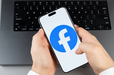 New York, ABD - 6 Nisan 2024: Akıllı telefon ekranındaki popüler Facebook mobil uygulaması dizüstü bilgisayarın klavye arka planında