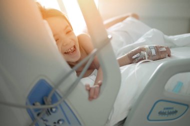 Hasta yatağında, hastalıktan IV tedavisi gören gülümseyen bir çocuk. 