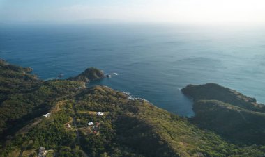 Okyanus kıyısındaki yeşil tepeler gün batımında hava aracı görüntüsü