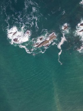 Üzerinde kayalar ve beyaz köpükler olan yeşil deniz suyu.