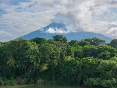 Yoğun ormanın üzerinde, bulutlarla örtülü, doğanın güzelliğini ve sükunetini aydınlatan devasa volkanlar beliriyor..