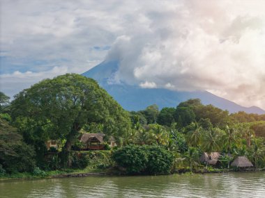 Bereketli bitki örtüsü, günbatımında gölgelerle örtülü volkan zeminiyle sakin nehri çevrelemektedir..