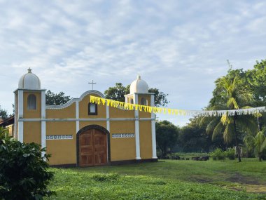Tuhaf sarı kilise parlak mavi gökyüzünün altında canlı yeşillikler arasında gururla duruyor. Huzurlu bir atmosferi çağrıştırıyor..