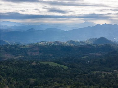 Uçsuz bucaksız yeşil tepeler ve dağlar bulutlu gökyüzünün altında doğanın güzelliğini gösteren sabahın erken saatlerinde harmanlanır..